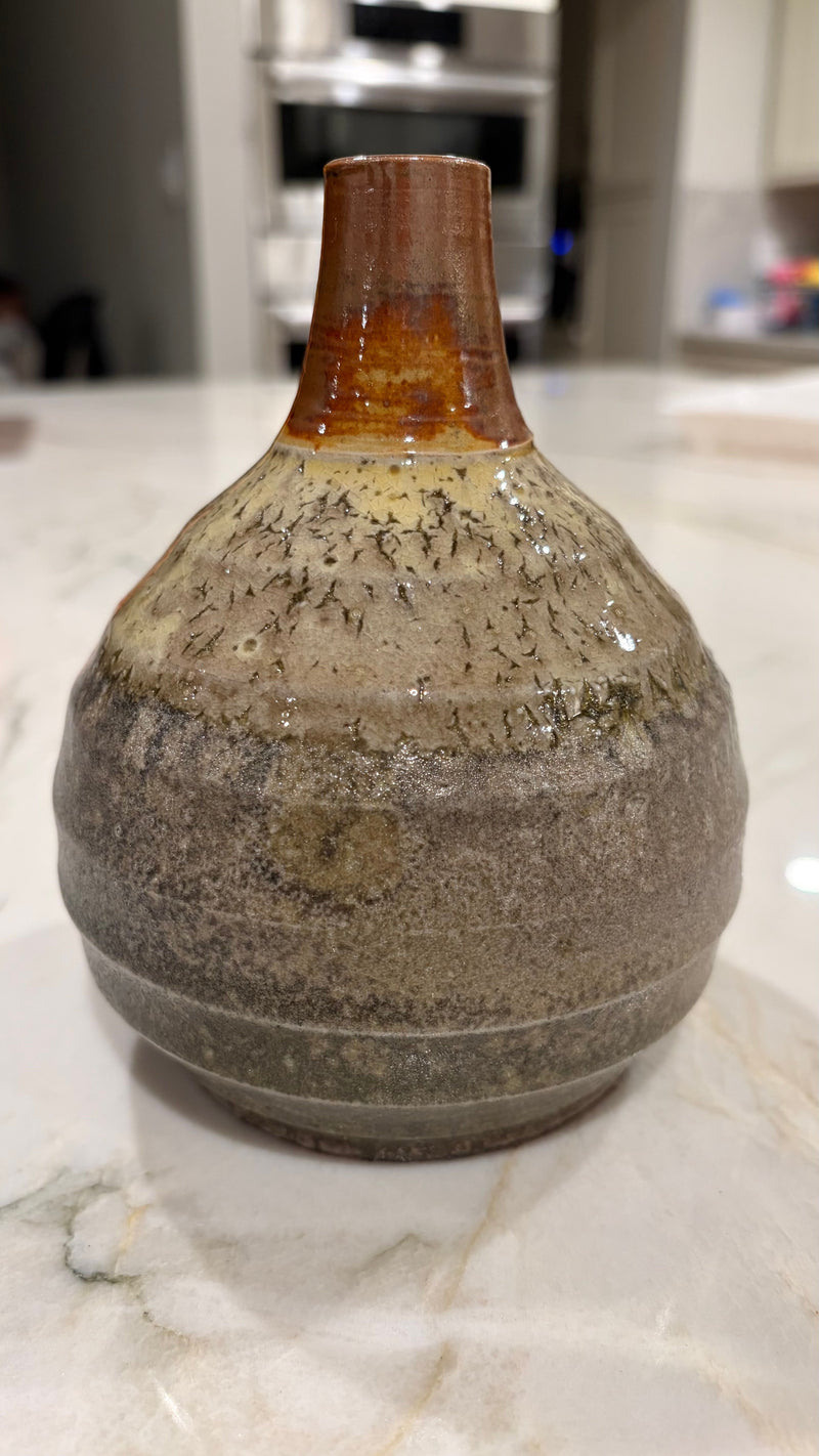 Sculptural stoneware vessel with bulbous form, mottled ash glaze body, and fired iron amber neck, showing deliberate carved horizontal lines at the base